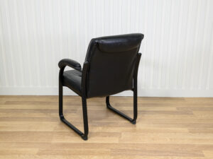 Chaise visiteur en similicuir noir avec structure en métal et des accoudoirs intégrés.